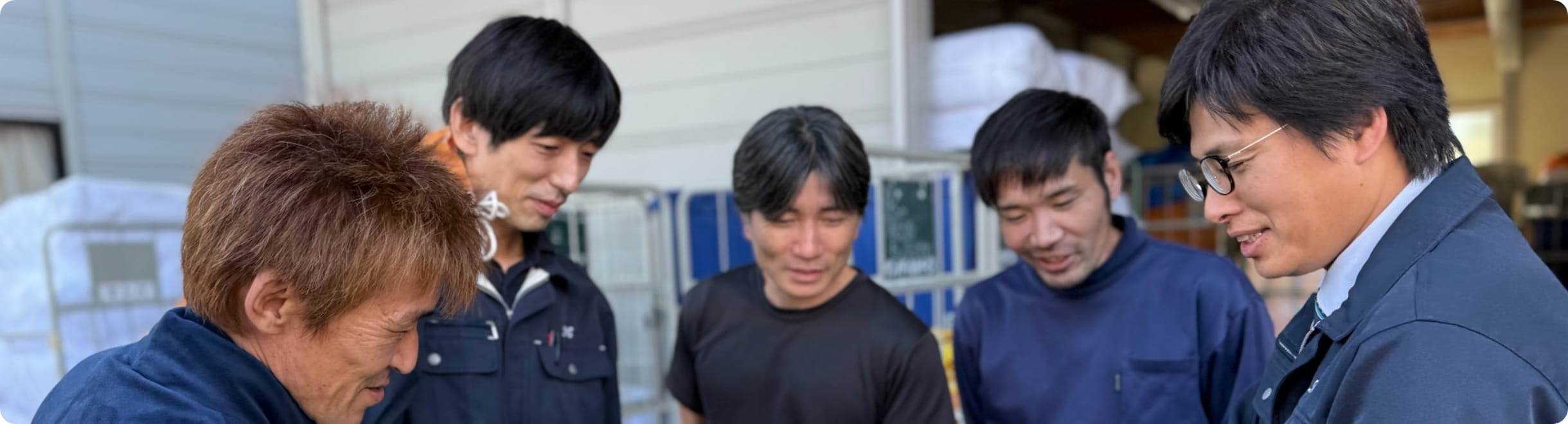 作業服を着たスタッフが集まり、書類を確認しながら打ち合わせをしている様子