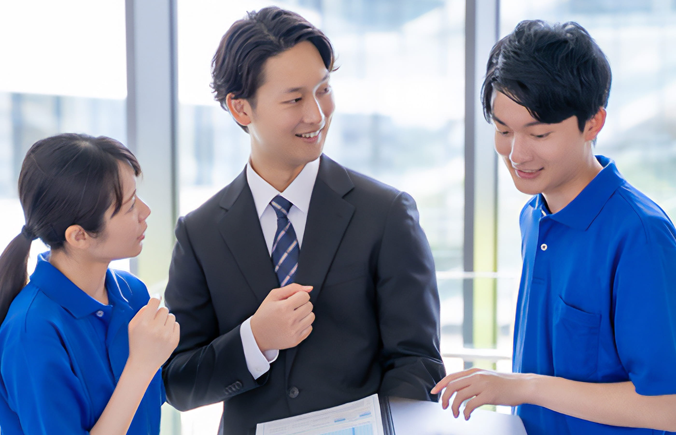 スーツ姿の男性が青い制服を着た2人のスタッフと打ち合わせをしている様子