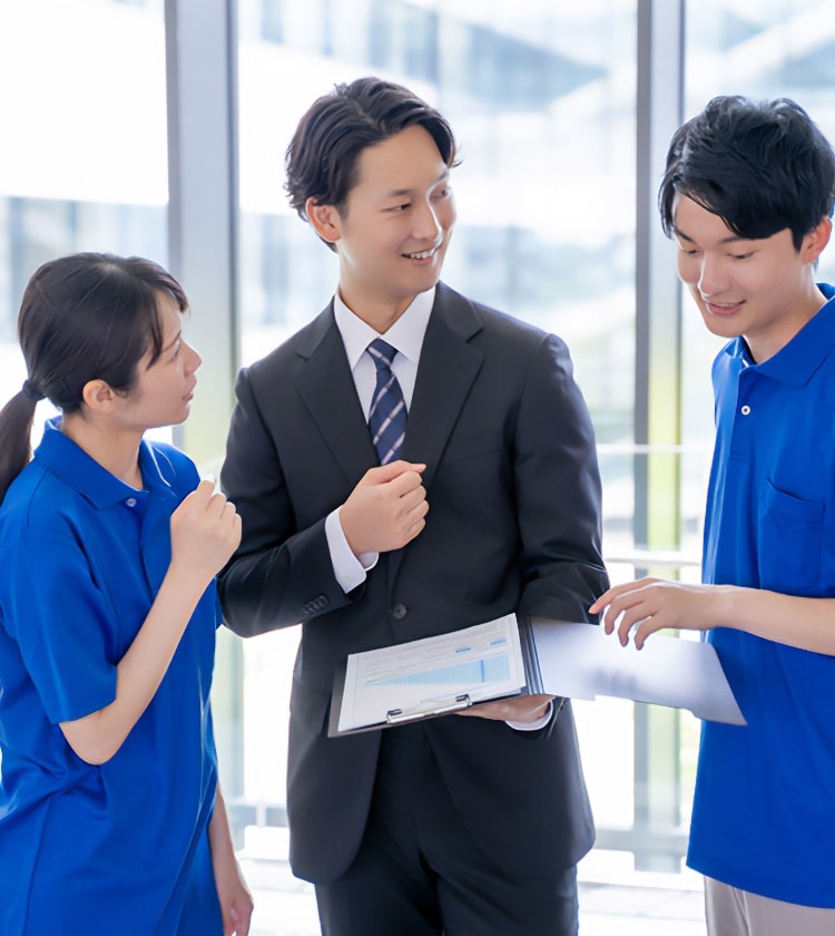 スーツ姿の男性が青い制服を着た2人のスタッフと打ち合わせをしている様子