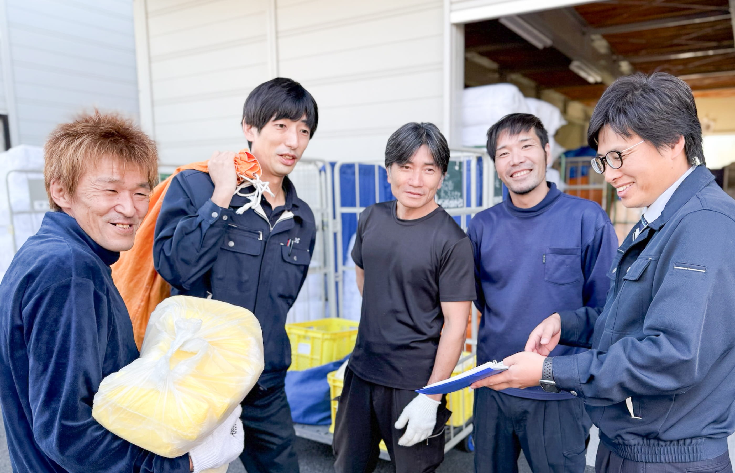 作業着を着た男性グループが笑顔で荷物を運びながら話している様子