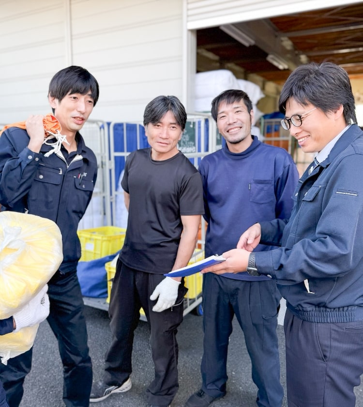 作業着を着た男性グループが笑顔で荷物を運びながら話している様子